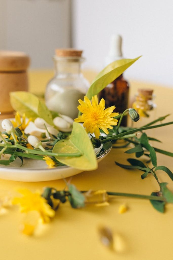 Close-up of herbal remedies featuring fresh flowers and essential oils on a yellow surface.